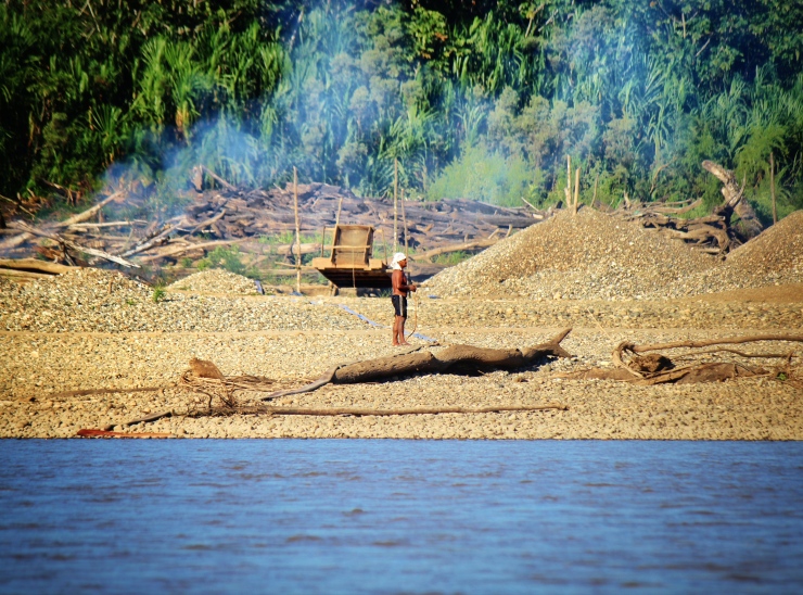 Mining standing in front of a caranchera (semi-mechanized mining equipment including motor and pump, sluice box, carpeted ramp for capturing gold flakes). During the dry season (especially July-September) it is common to see smoke along beaches, where felled trees and gathered driftwood (locally referred to as palizada) incinerated to make space for mining sites.