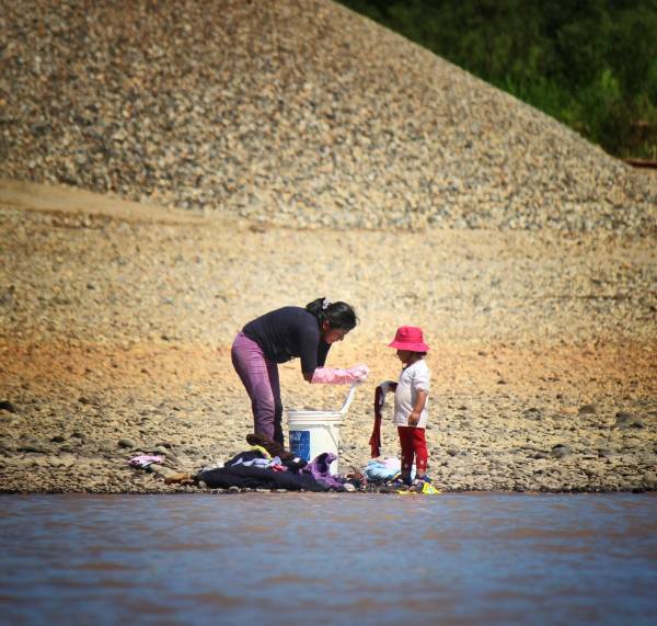 A young child helps her mother wash clothes for Miners on the Madre de Dios River